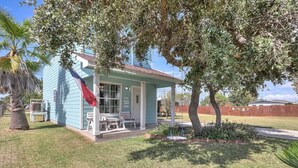 A small, light blue house with a porch, surrounded by grass and trees. - G & J Paradise (Rockport)