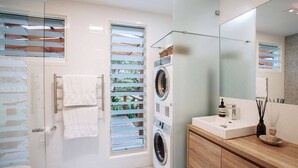 Een moderne badkamer met een glazen douchecabine, een ingebouwde wasmachine en een houten wastafelmeubel met een wastafel.
