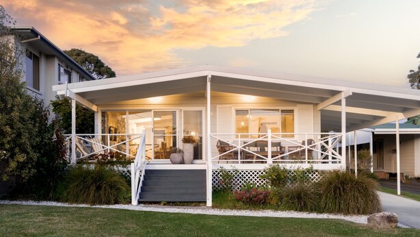 Een modern huis met een overdekte veranda, een trap naar de ingang en een verzorgde tuin.