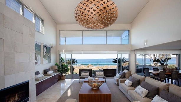A spacious living room with a fireplace, large windows, and a view of the beach. - 'Atra' - Jervis Bay Beach Front Holiday Home (Callala Beach)
