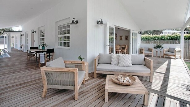 A spacious outdoor deck with wooden flooring, a sofa, chairs, and a dining table.
