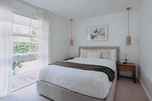 Ein Schlafzimmer mit einem großen Bett, einem Nachttisch, einer Hängelampe und einem Fenster mit durchsichtigen Vorhängen.