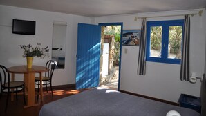 Una habitación con cama, una mesa con sillas, televisor y ventana con cortinas.