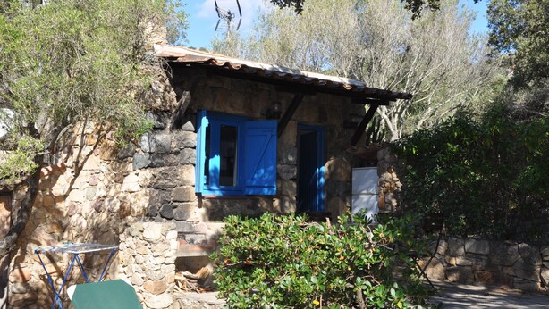 Un edificio de piedra con contraventanas azules, una pequeña mesa y una silla verde.