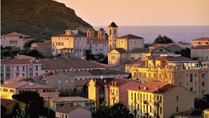 Un pueblo costero con edificios históricos, incluyendo una iglesia con campanario, y vistas al mar.