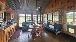 A rustic cabin interior with a dining table, chairs, a sofa, and a kitchen area. - Camplee - 50 Acres of Freedom (Zavalla)