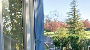 A window with a view of a garden, including a lawn, trees, and a blue door. - Rent this charming furnished studio near Rocamadour and Padirac  (Gramat)