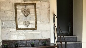 A rustic stone wall with a framed decorative piece and a wicker chair. - Rent this charming furnished studio near Rocamadour and Padirac  (Gramat)