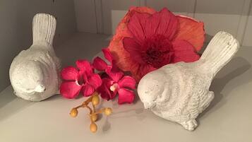 Three white ceramic sculptures, one of which is a rabbit, placed on a flat surface with a large red flower and smaller pink flowers in the foreground.