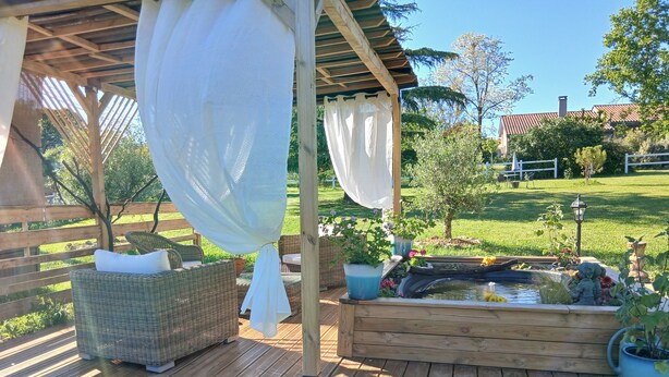 A wooden deck with wicker furniture, a small pond, and potted plants. - Rent this charming furnished studio near Rocamadour and Padirac  (Gramat)