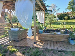 Um deck de madeira com móveis de vime, um pequeno lago e plantas em vasos.