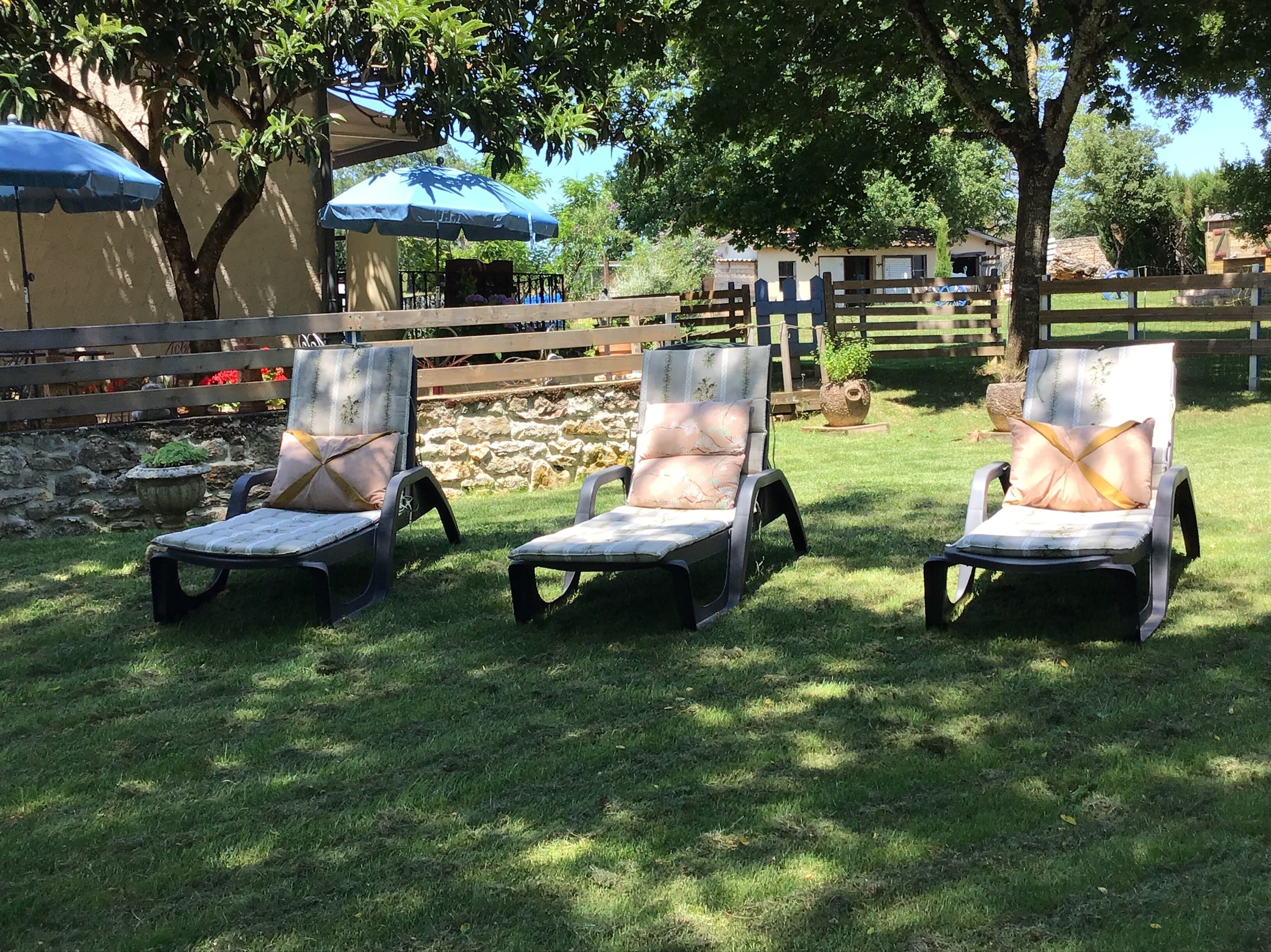 Drei Loungesessel mit Kissen, eine Steinmauer und ein Holzzaun in einem Garten.