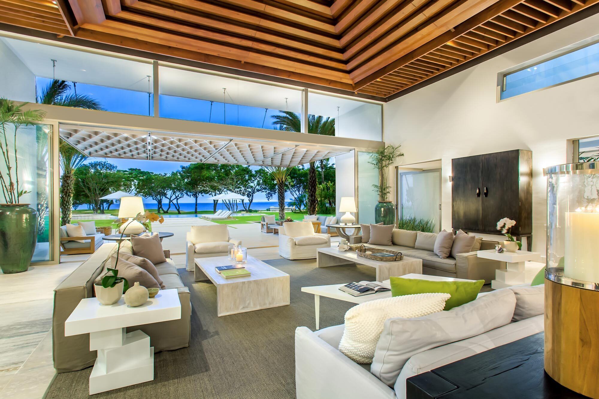 A modern living room with a view of the ocean, featuring a sofa, coffee tables, and a large cabinet.