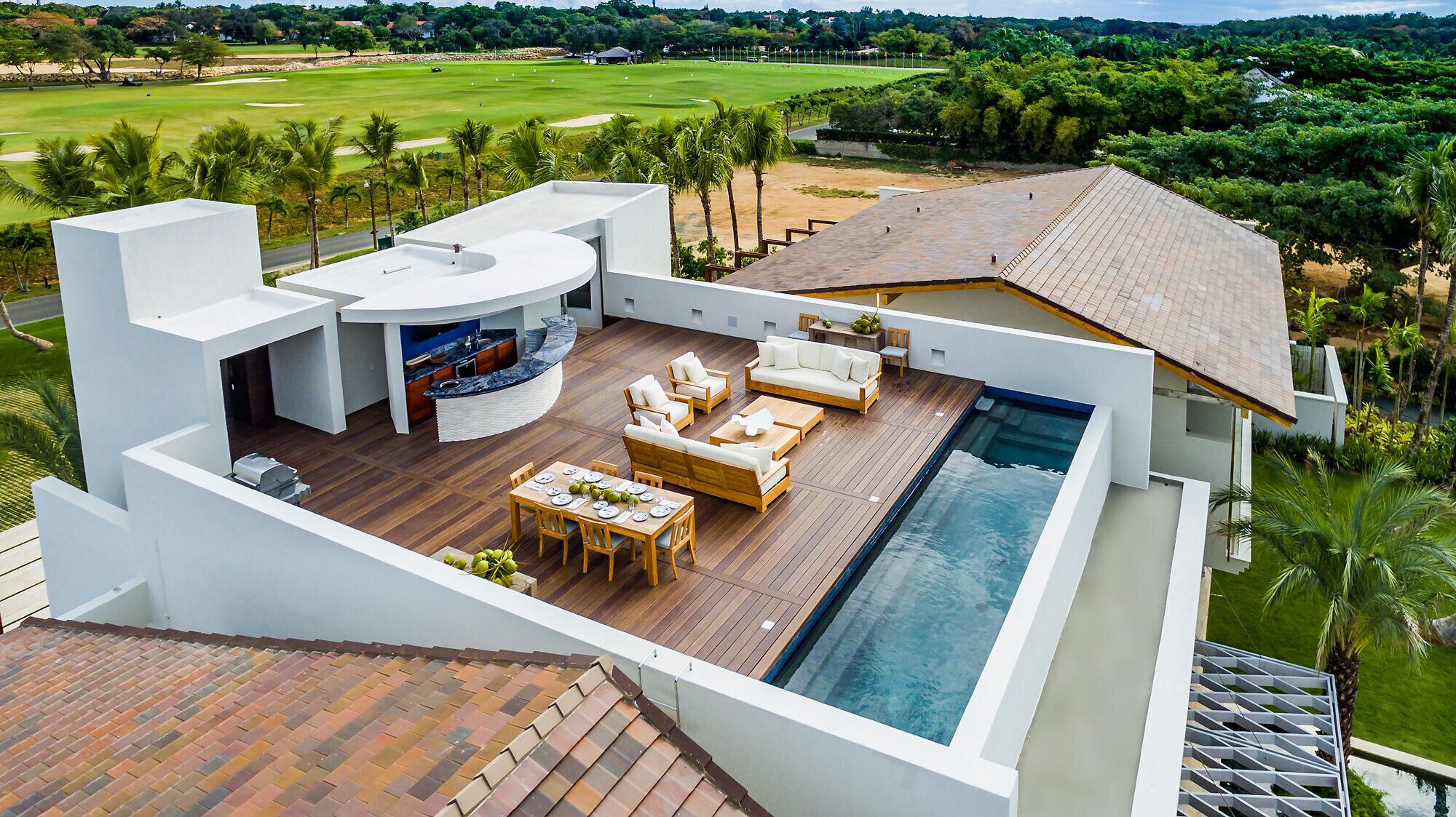 A modern outdoor living area with a pool, wooden furniture, and a kitchen.