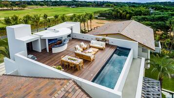 A modern outdoor living area with a pool, wooden furniture, and a kitchen.