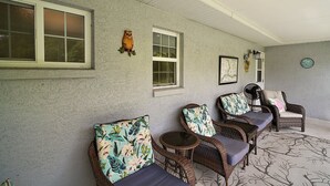 Un patio cubierto con mobiliario de mimbre y asientos acolchados, que incluye una pared con textura y decoración mural.