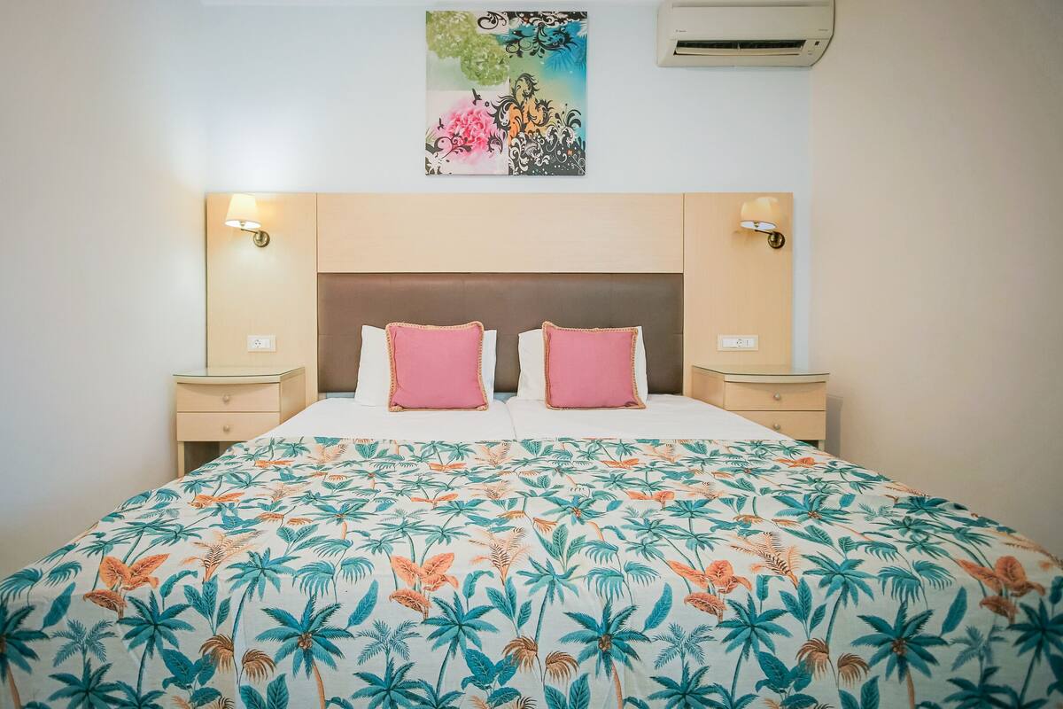 A hotel room with a bed, two nightstands, a headboard, and a wall-mounted air conditioner.
