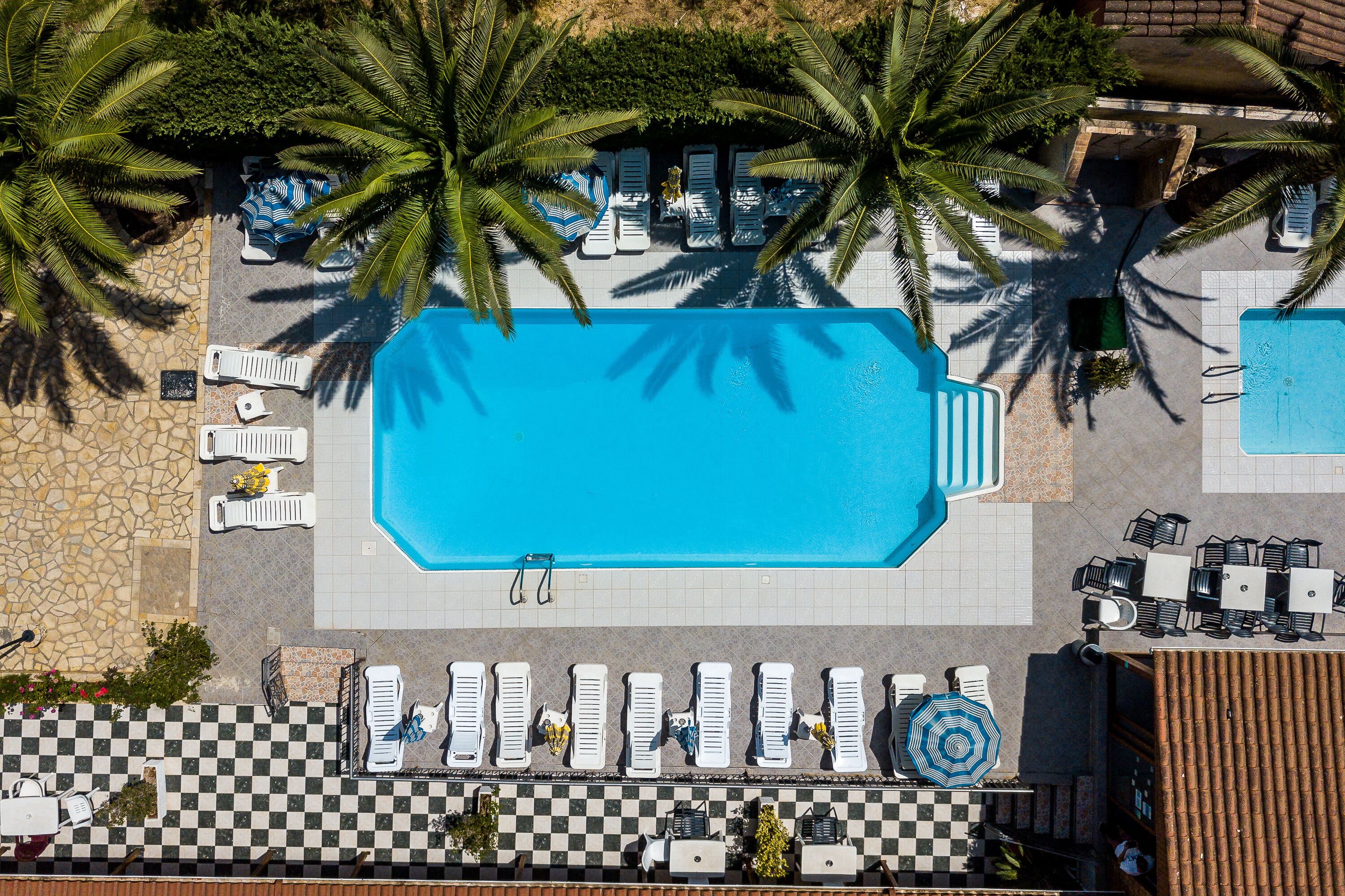 An aerial view of a pool area with lounge chairs, a checkered floor, and palm trees.