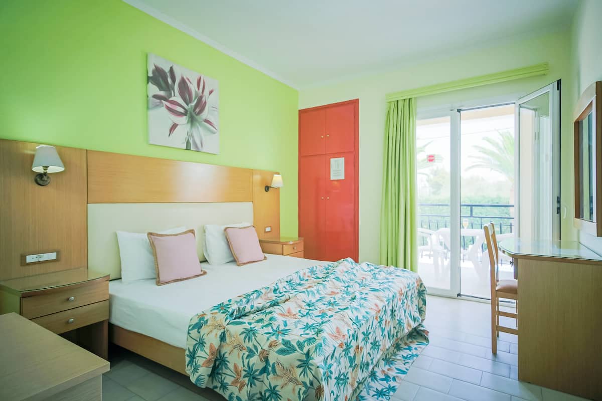A hotel room with a bed, a desk, a chair, a nightstand, and a door leading to a balcony.