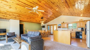 A spacious living area with a wooden ceiling, a dining table, and a kitchen with wooden cabinets and a refrigerator.