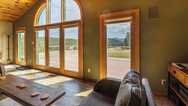 A spacious room with a large wooden ceiling, a leather sofa, a wooden table with wooden coasters, and large arched windows offering a view of a green landscape.