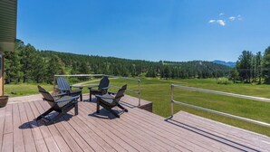 A deck with two chairs and a table, overlooking a green landscape with trees and a road.