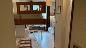 Une chambre d’hôtel compacte comprenant un lit superposé, une petite kitchenette et un coin salon séparé.