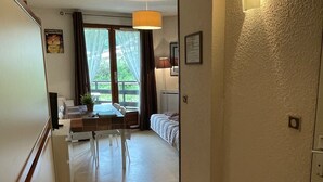Une chambre d’hôtel compacte dotée d’une kitchenette, d’un coin repas avec une table et des chaises, d’un canapé et d’une grande fenêtre donnant sur un paysage verdoyant.
