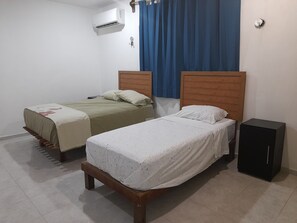 A bedroom with two beds, a wooden headboard, a black cabinet, and an air conditioning unit.