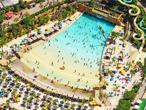 An aerial view of a large indoor swimming pool with multiple lanes, surrounded by sun loungers and umbrellas.