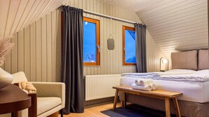 Ett mysigt sovrum med en säng, ett litet bord, en stol och två fönster med gardiner.