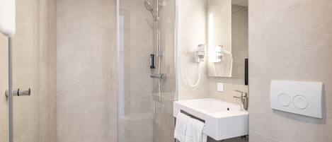 A modern bathroom with a glass shower enclosure, a white sink, and a mirror.
