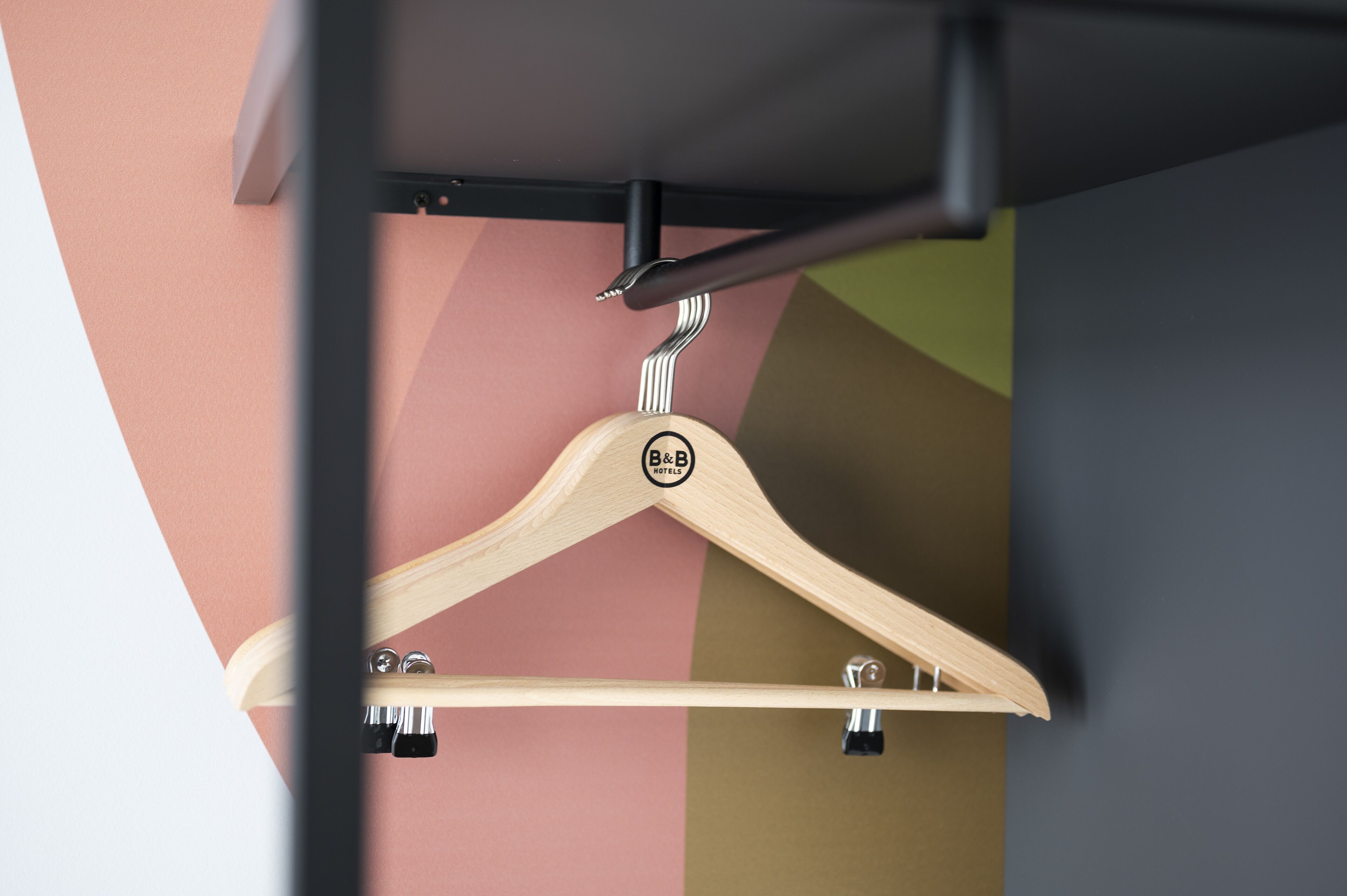 A wooden hanger with a logo, attached to a metal rod, against a multicolored wall.
