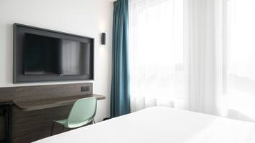 Een hotelkamer met een bed, een aan de muur bevestigde televisie, een bureau met stoel en een raam met gordijnen.