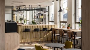 A modern bar area with high stools, a wooden counter, and a city view through large windows. - B&B HOTEL Antwerpen Centrum (Antwerp)