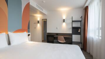A hotel room with a large bed, a desk, a chair, and a wardrobe.