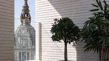 Un edificio con una estructura abovedada y una aguja, junto a un muro de ladrillo blanco y una planta en maceta.