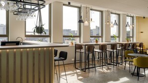 A modern cafe with a bar area, multiple seating options, and large windows offering city views. - B&B HOTEL Antwerpen Centrum (Antwerp)
