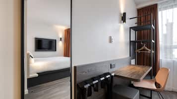 A modern hotel room with a bed, a TV, a desk, and a chair.