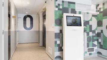 Un pasillo moderno de hotel con un quiosco digital de información, ascensores y un diseño de pared geométrico.