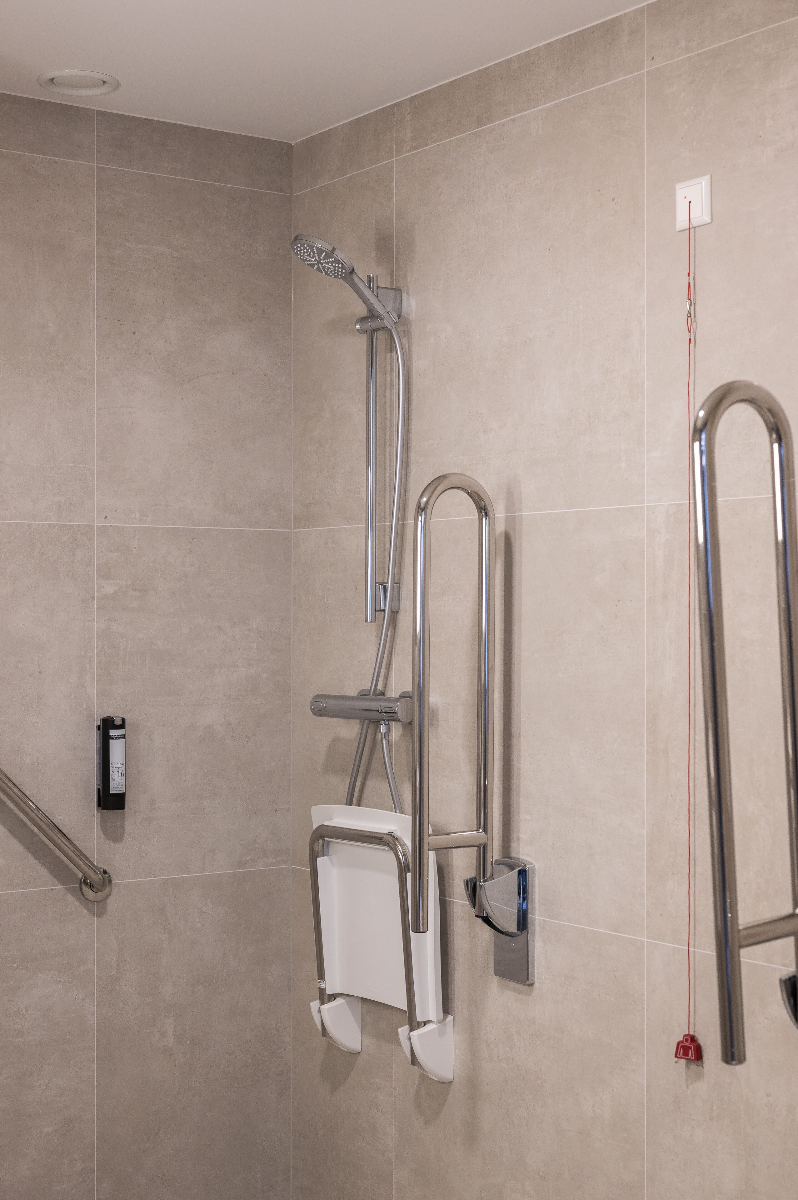 A shower area with a handheld showerhead, grab bars, and a wall-mounted faucet.
