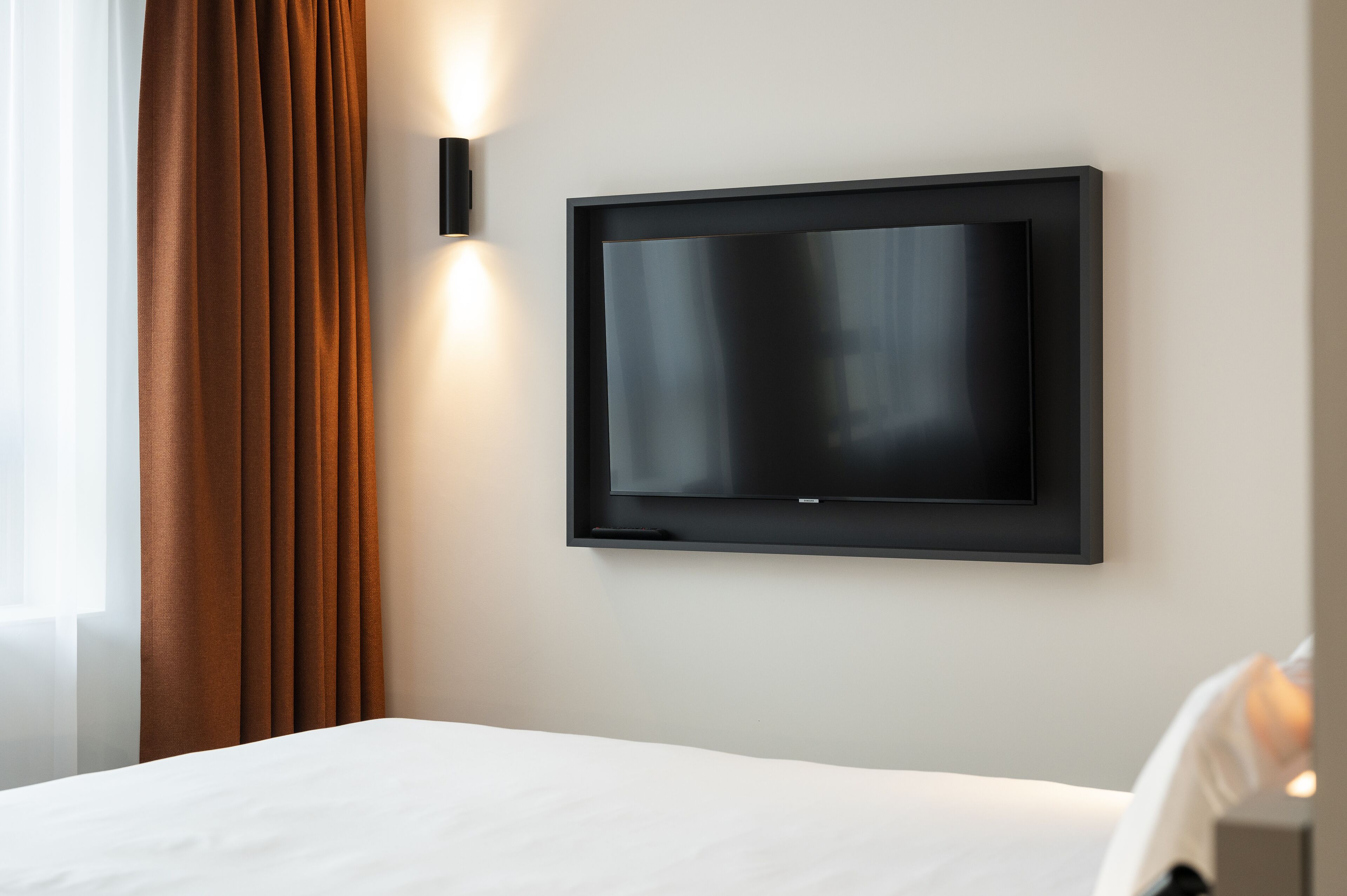 A hotel room with a bed, a mounted TV, and a window with curtains.
