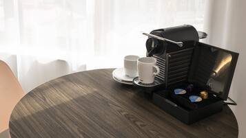 Una mesa redonda de madera con una máquina de café, dos tazas blancas y una bandeja con una caja pequeña y un objeto azul.