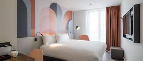 Una habitación de hotel moderna con una cama grande, un escritorio con una silla, un televisor de pantalla plana y un ventanal con cortinas.