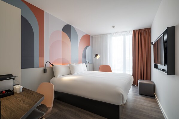 A modern hotel room with a large bed, a desk with a chair, a flat-screen TV, and a large window with curtains.