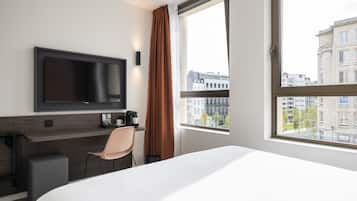 Une chambre d’hôtel avec un lit, un bureau et une chaise, une télévision et une fenêtre donnant sur la ville.