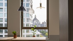 A room with a large window, two potted plants, a wooden table, and two hanging lamps. - B&B HOTEL Antwerpen Centrum (Antwerp)