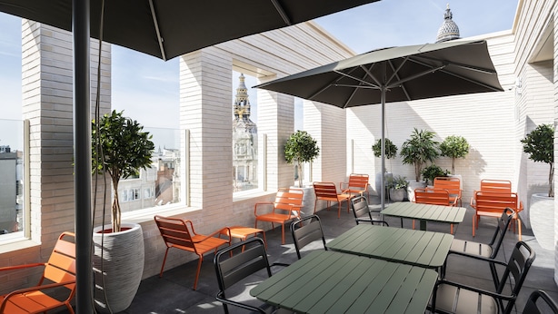 An outdoor patio with tables and chairs, potted plants, and a view of a building with a dome. - B&B HOTEL Antwerpen Centrum (Antwerp)