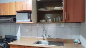 A kitchen with wooden cabinets, a microwave, a sink, and a stove. - A cozy apartment located in the heart of surco  (Lima)