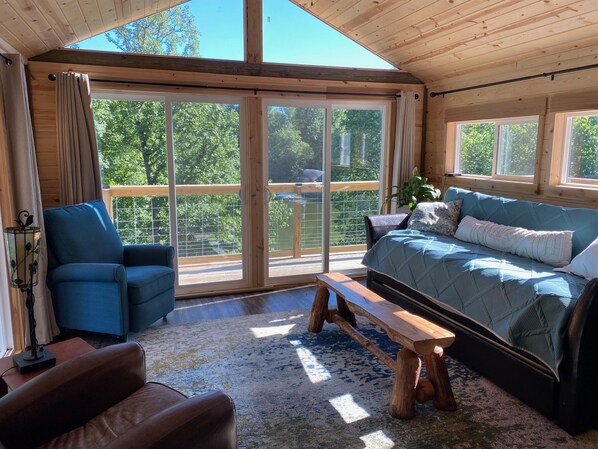 A cozy room with a large window, a blue sofa, a wooden bench, and a leather chair.